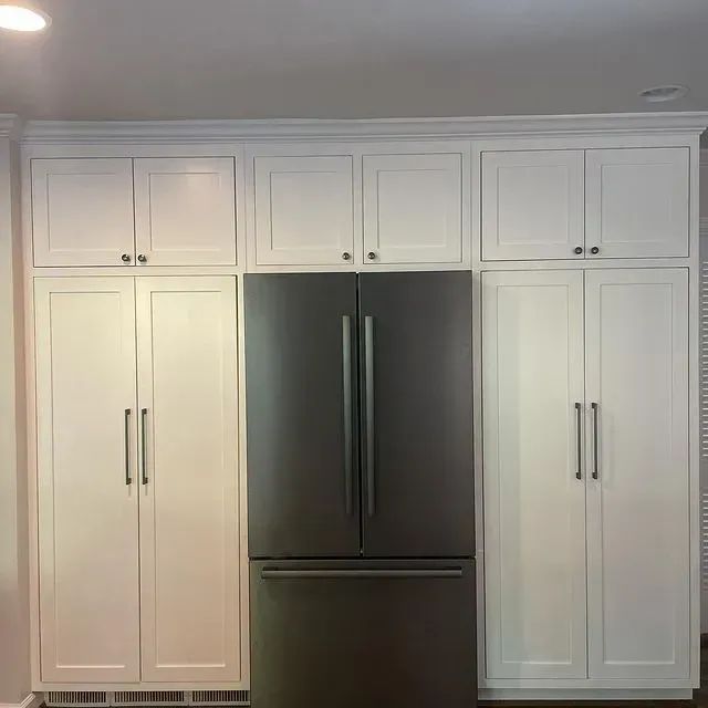 White kitchen wall with built-in cabinets and a stainless steel French-door refrigerator in the center