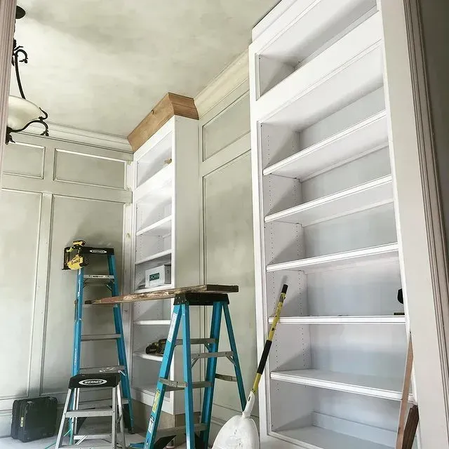 Ladder-filled room with tall white built-in shelves under construction and tools on the floor