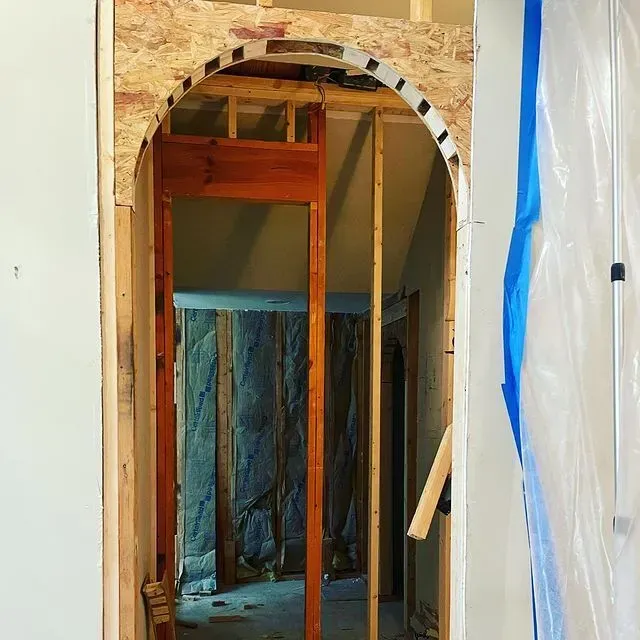 Partially demolished wall with exposed studs and an arched opening in a renovation site