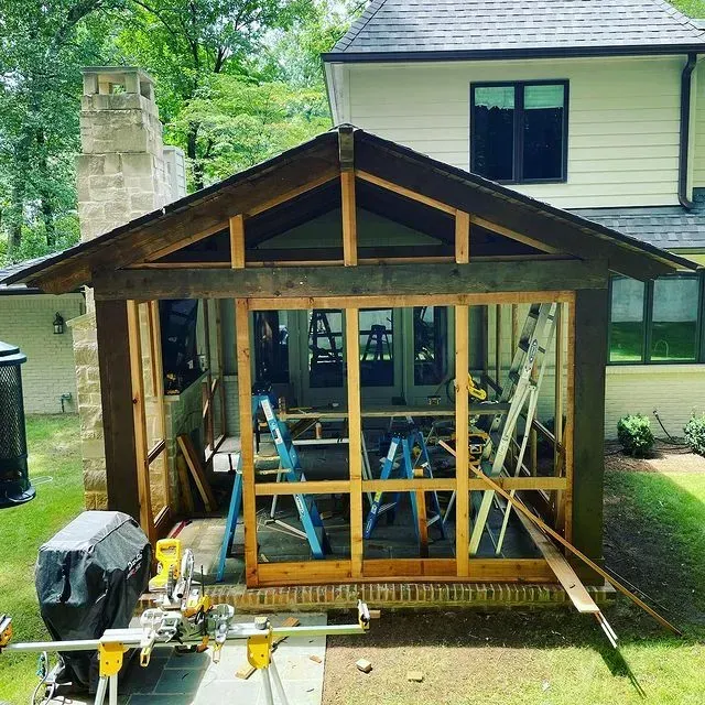 Partially built wooden porch addition with exposed framing beside a house in a backyard