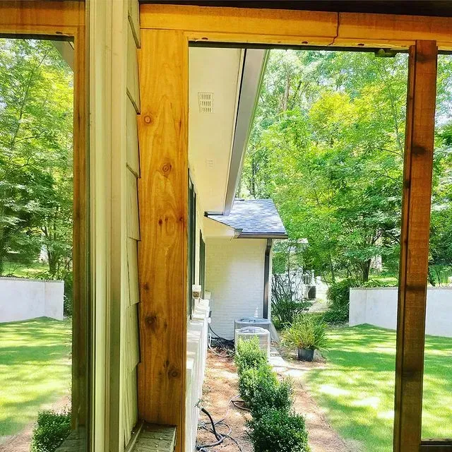 Wooden doorway framing a sunny garden path with shrubs, lawn, and trees beyond.