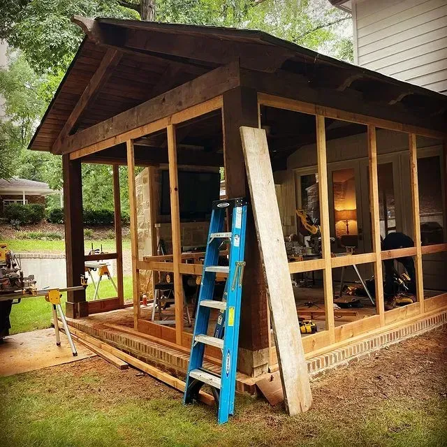 Wooden shed under construction with blue ladder and open walls in a wooded yard
