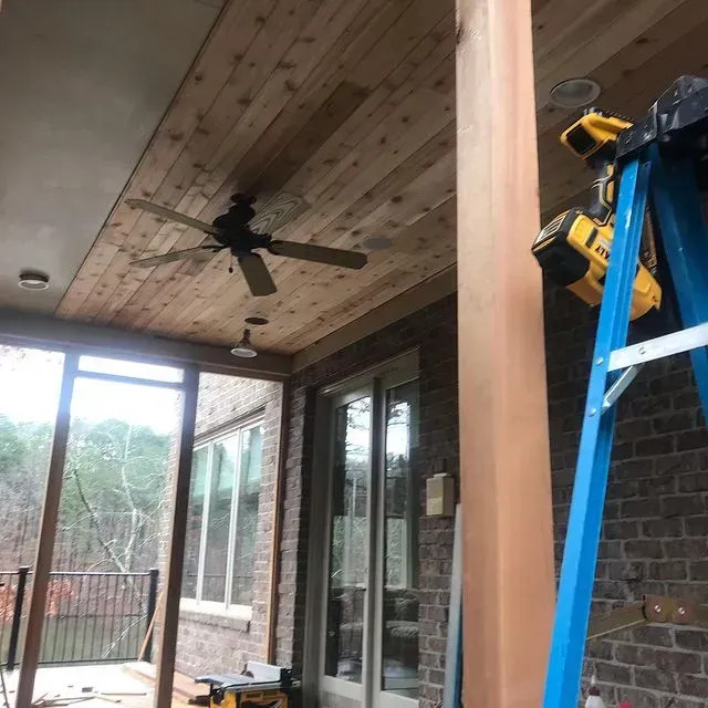 Covered patio with wood ceiling, ceiling fan, sliding glass doors, and a blue ladder beside a brick wall