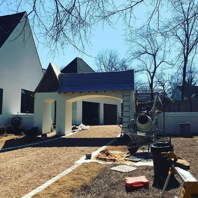 Backyard construction site with a white pavilion, gravel path, ladder, and tools under a blue sky