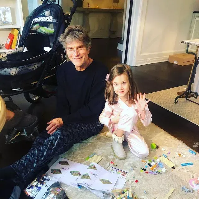 A man and a young girl sit on the floor amid scattered craft supplies, smiling at the camera.
