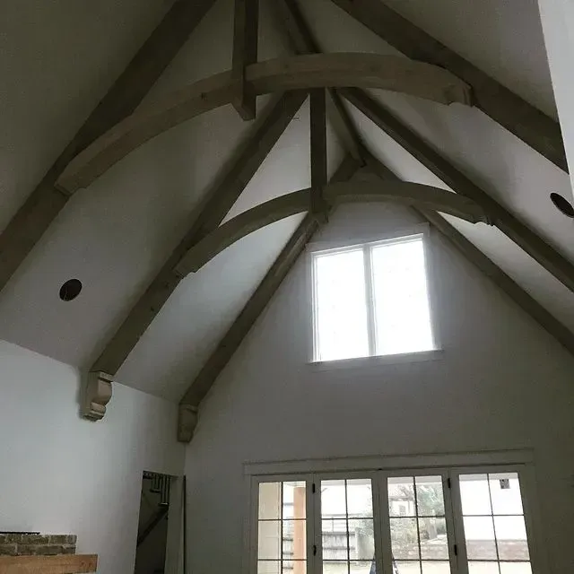 White vaulted room interior with exposed wooden beams and a bright window above French doors