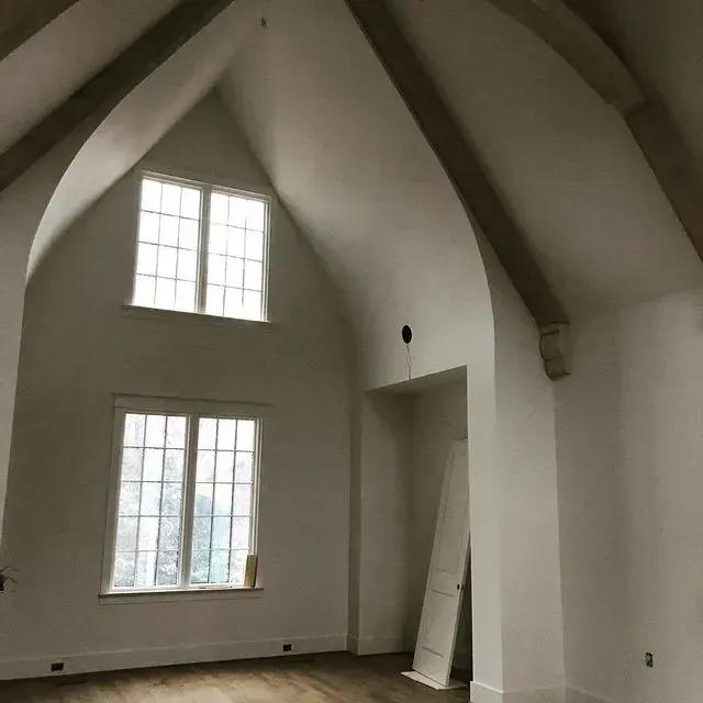 Empty room with vaulted ceiling, two tall windows, and white walls under renovation