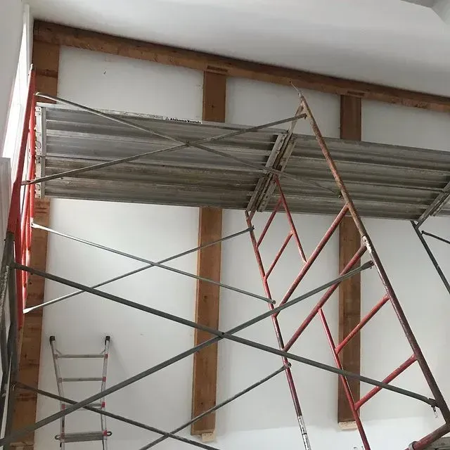 Red-and-silver scaffolding inside a room under construction, with exposed wooden wall framing.