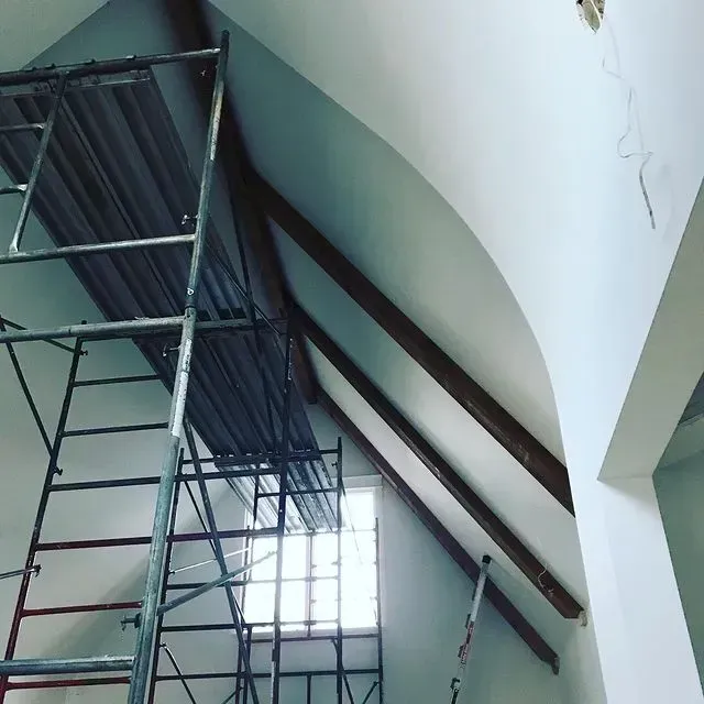 Scaffolding inside a room with a high slanted ceiling and arched white walls