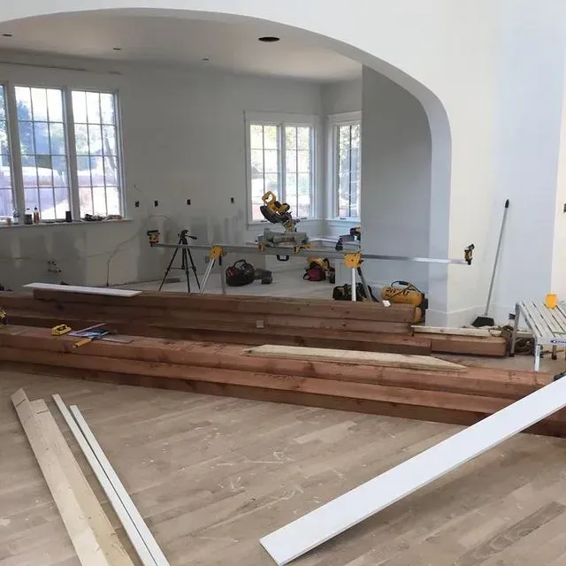 Renovation in progress in a bright room with wood beams, tools, and windows overlooking outside.
