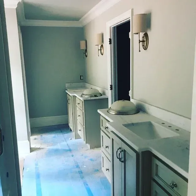 Long bathroom with twin white vanities, wall sconces, and a blue-painted back wall