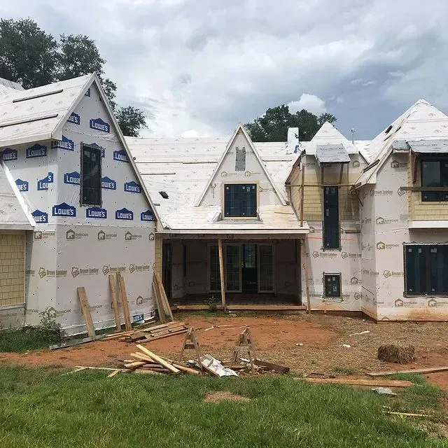 Partially built house with exposed framing, white roof sheathing, and construction debris in front