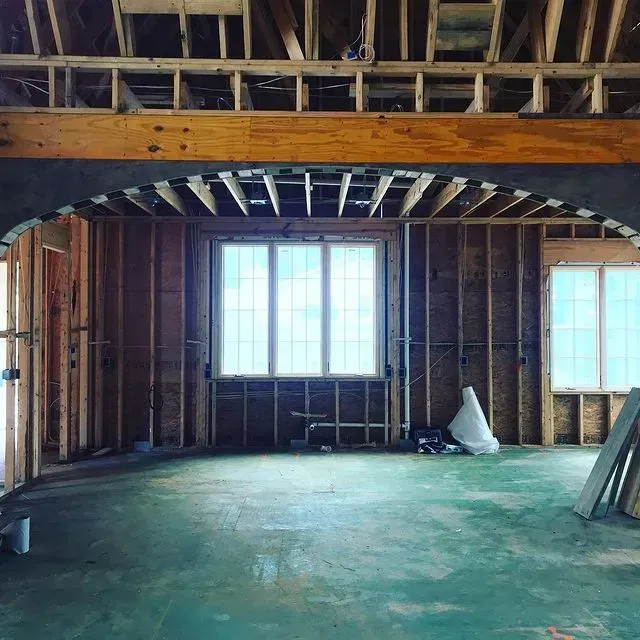 Unfinished room with exposed wooden framing, large windows, and green floor under construction