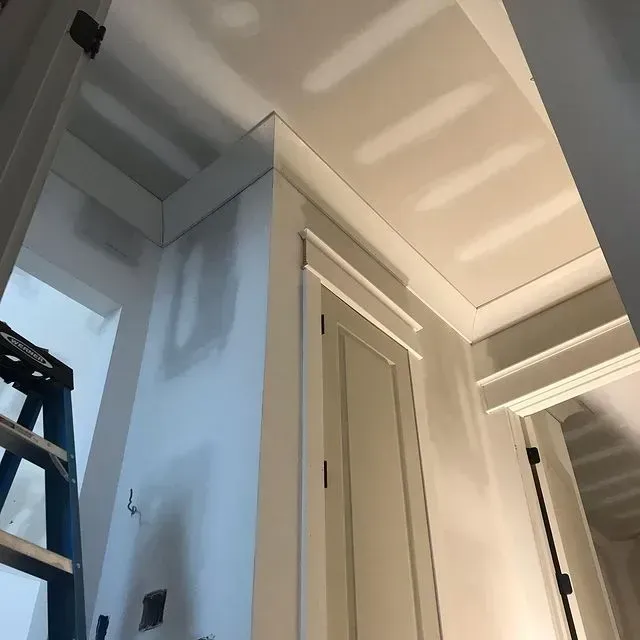 Interior hallway with white doors, ceiling trim, and a ladder at the left edge.