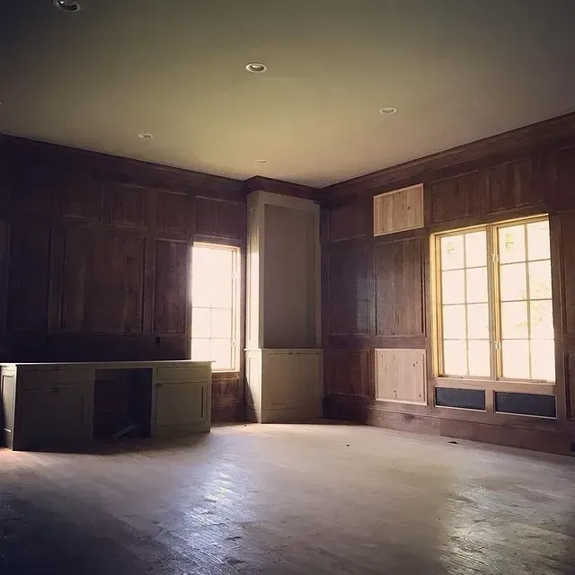 Empty wood-paneled room with large windows and bare floor, lit by soft daylight