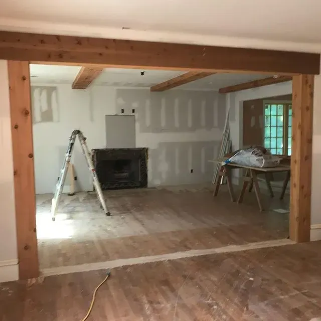 Empty room under renovation with ladder, unfinished drywall, exposed beams, and hardwood floors