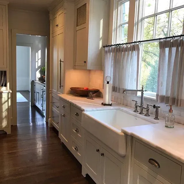 Bright white galley kitchen with farmhouse sink, long windows, and hardwood floors