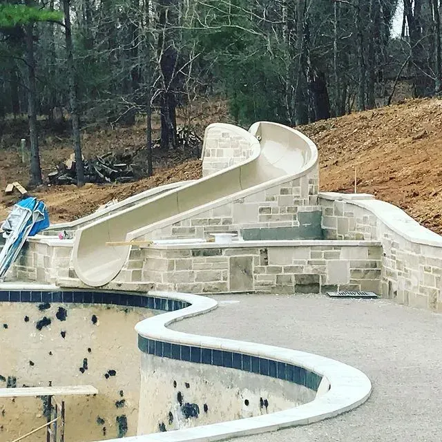 Curved concrete slide under construction in a wooded park setting