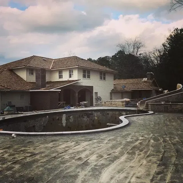Empty drained swimming pool in a backyard behind a two-story house under cloudy skies