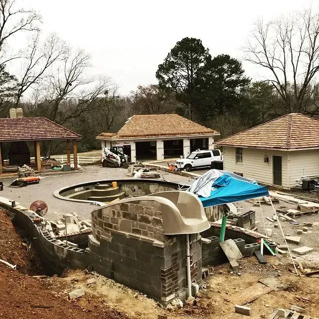 Storm-damaged residential area with collapsed brick wall, debris, and damaged garages under overcast sky