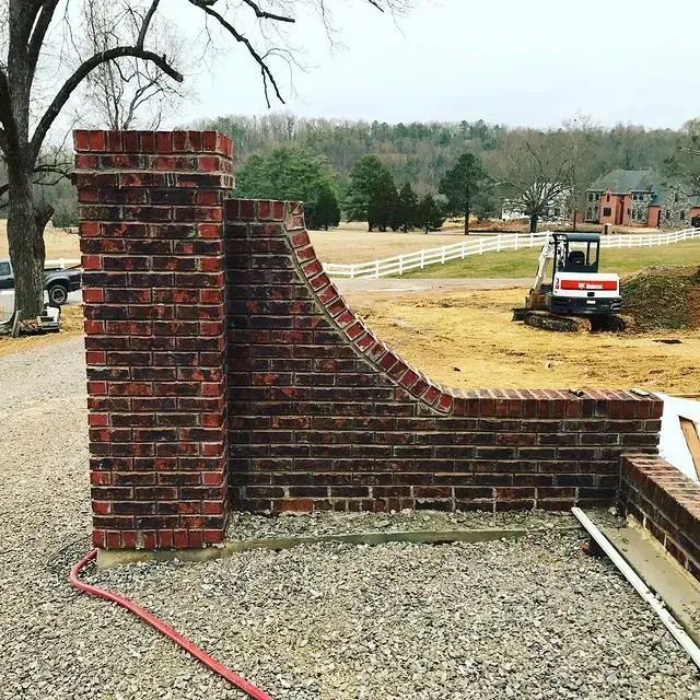 Partially built brick retaining wall beside gravel drive, with a white utility vehicle and yard in the background