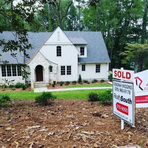White house with a SOLD real estate sign in the front yard, surrounded by trees