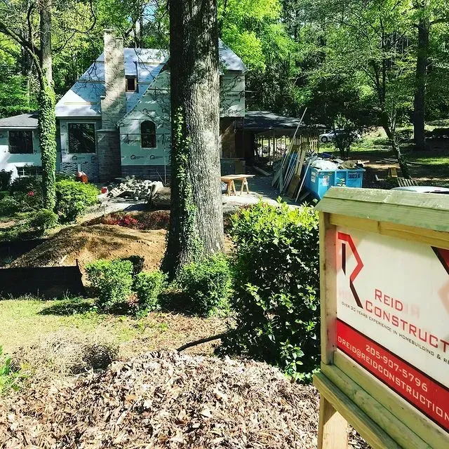 House under construction in wooded yard, with tree stump and Red Construction sign in foreground