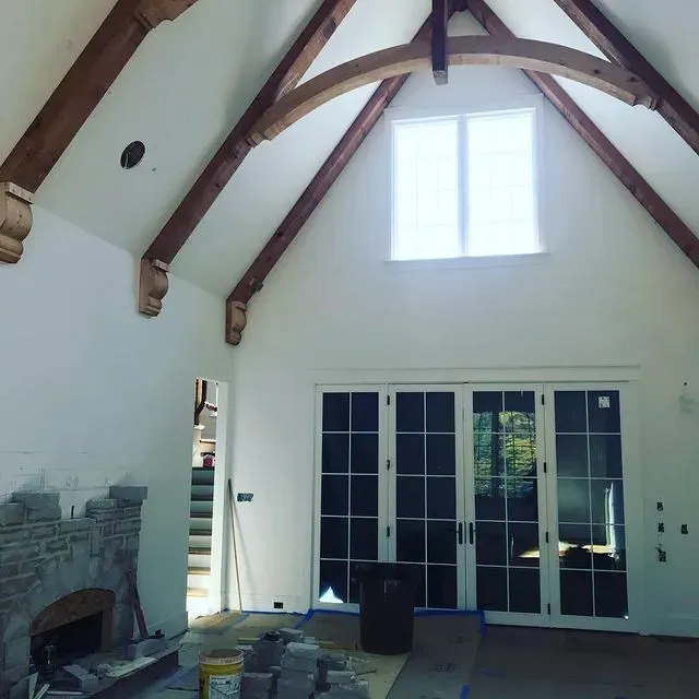 Spacious living room with vaulted wood-beam ceiling, fireplace, French doors, and a central window