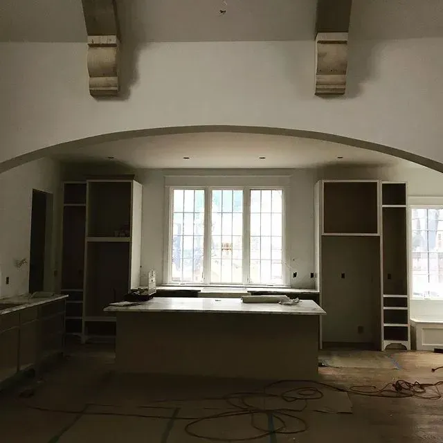 Renovated kitchen with white cabinets, large window, and unfinished floor, cords scattered around.