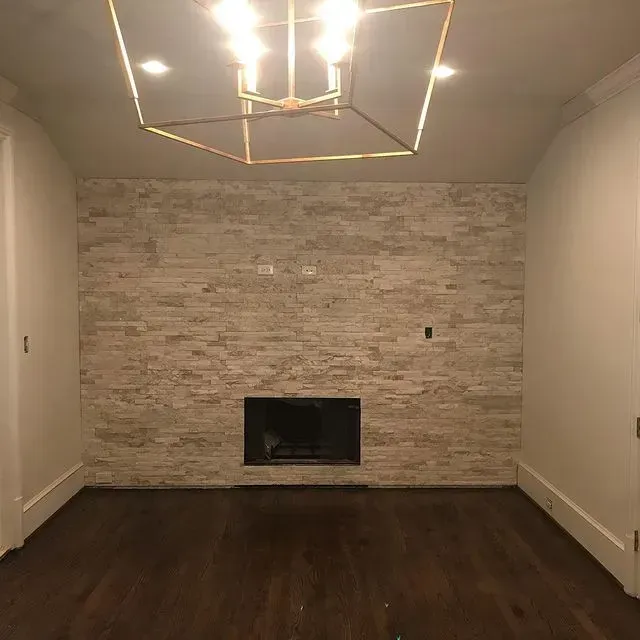 Empty modern living room with dark wood floors, stone accent wall, and geometric ceiling light.