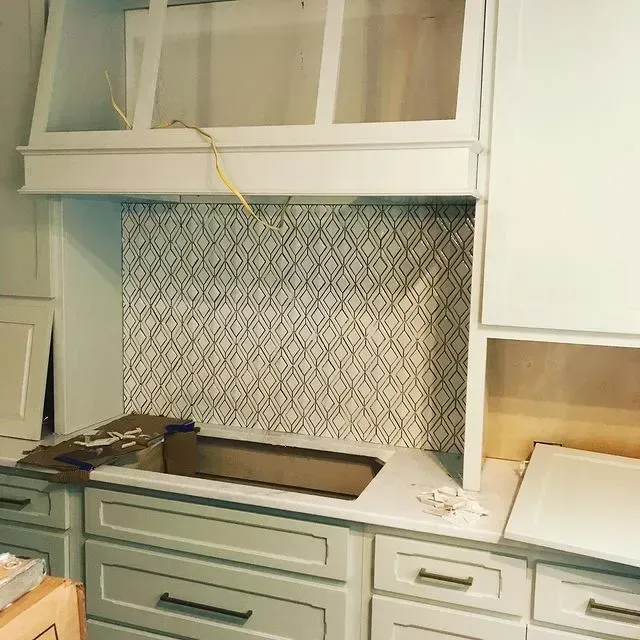 Kitchen under renovation with patterned backsplash, white cabinets, and green lower drawers