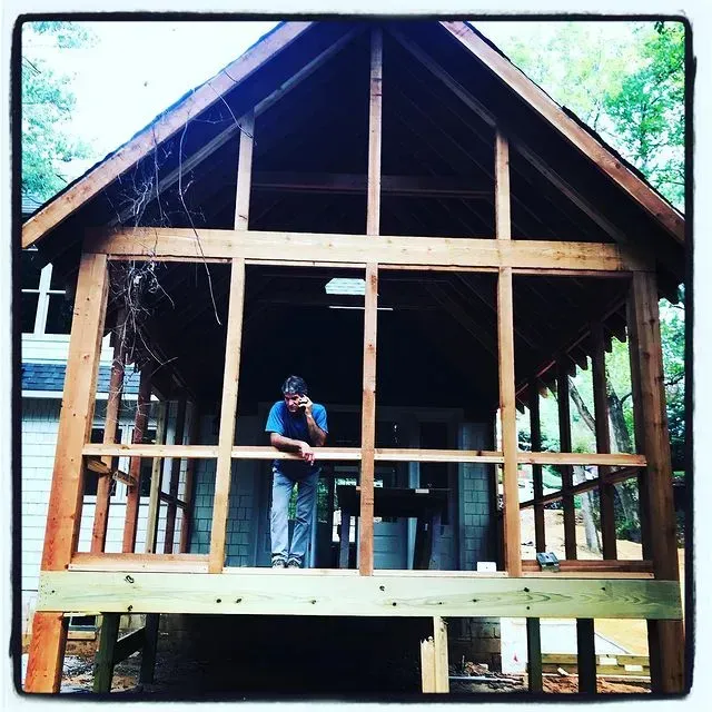 Partially built wooden cabin frame with a worker standing inside the front porch