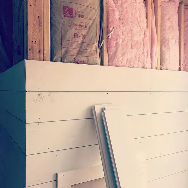 Stacked white boards leaning against insulated wall studs in an unfinished room