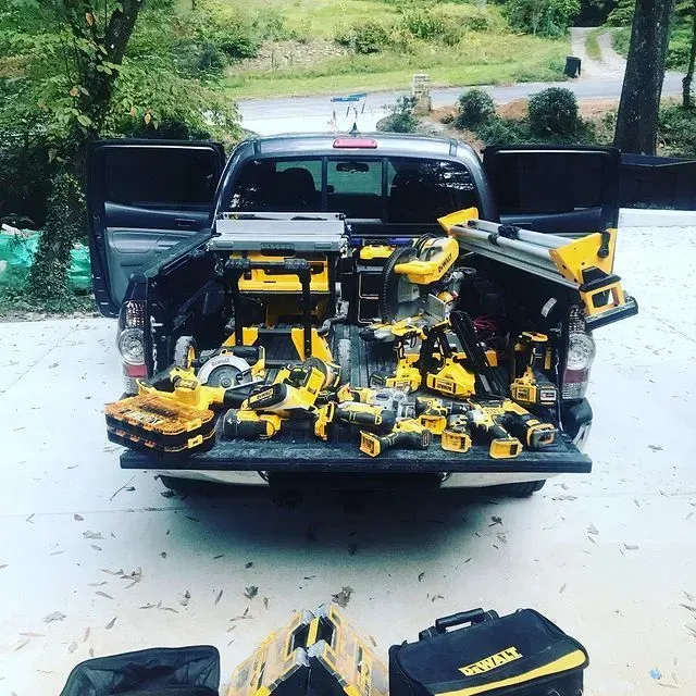 Open truck bed filled with yellow and black power tools outdoors on a driveway