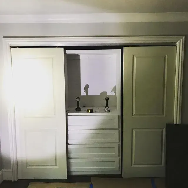 Open closet with sliding doors, revealing a white dresser and lamp in a small room.