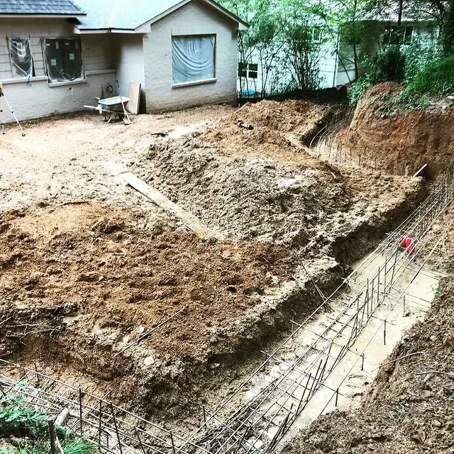 Backyard construction site with excavated dirt, trenches, rebar, and a house in the background