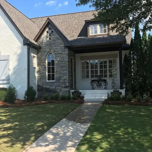 Stone-front house with arched window, covered porch, and front walkway under a sunny sky