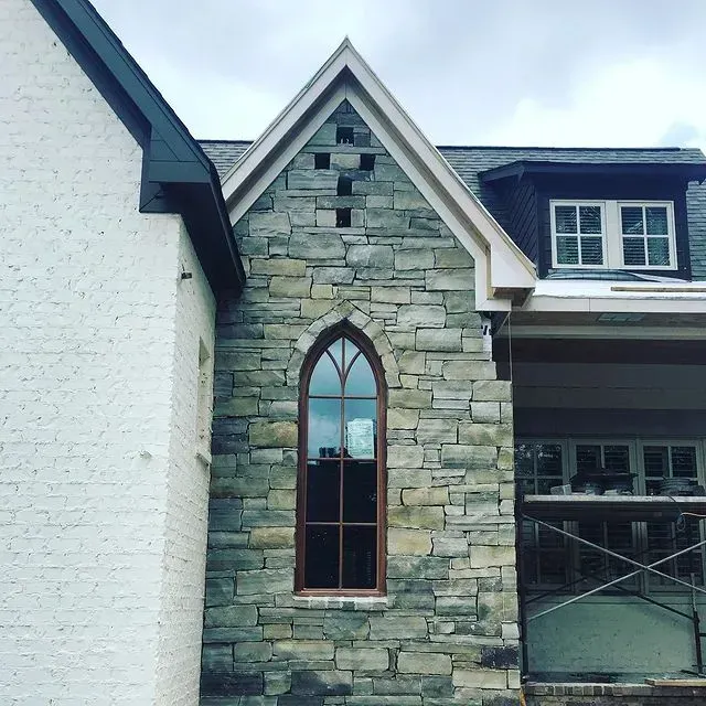Stone building facade with arched window beside a white wall and covered porch under construction