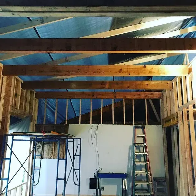 Interior construction site with exposed wooden beams, ladder, scaffolding, and hanging wires