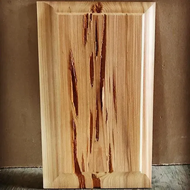 Wooden cutting board with light grain and dark streaks, standing upright against a brown background