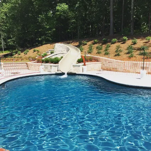 Blue swimming pool with a curved waterslide and wooded hillside in the background