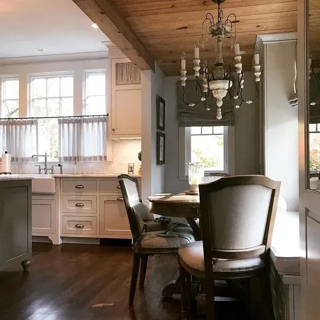 Bright kitchen and dining area with wood ceiling, chandelier, dark table, and white cabinets