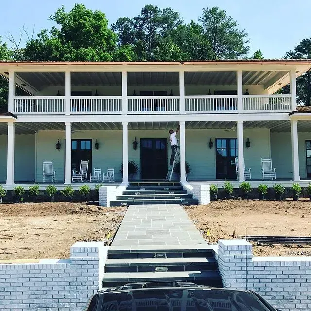 Two-story white house with front porch, central stairs, and a person standing in the doorway.