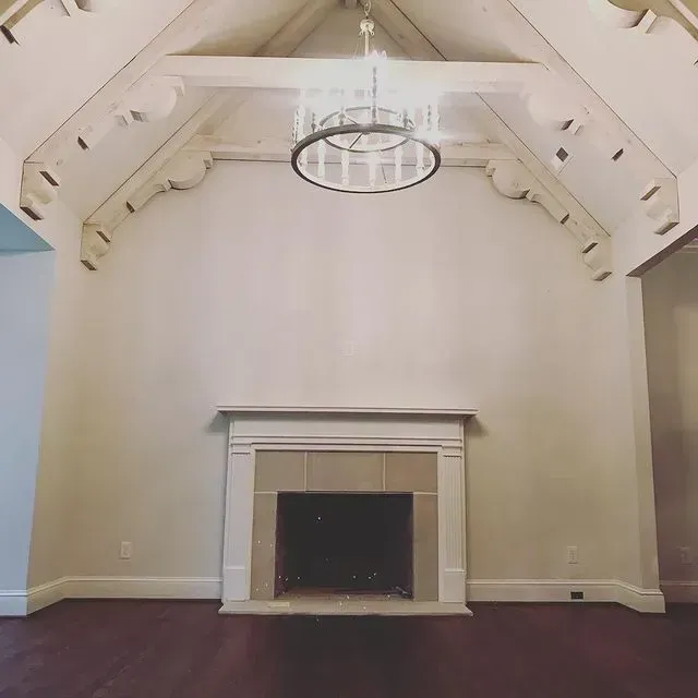 Empty room with vaulted white ceiling, central fireplace, and dark hardwood floor