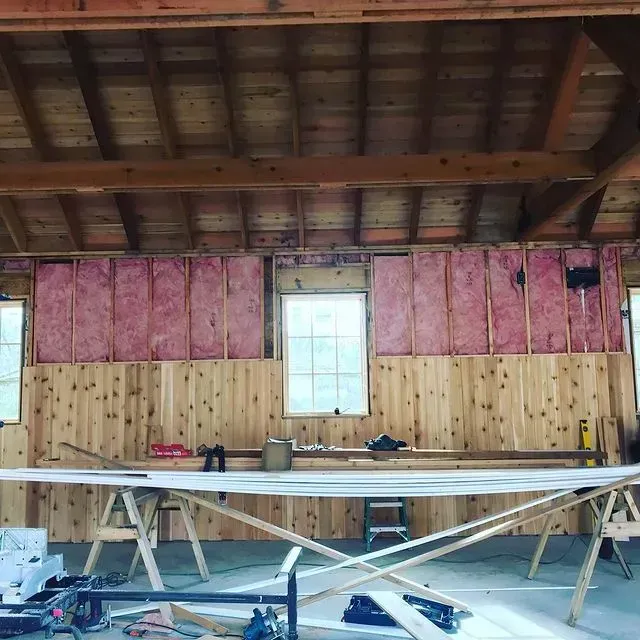 Workshop interior with exposed rafters, pink insulation walls, and a long table in the foreground
