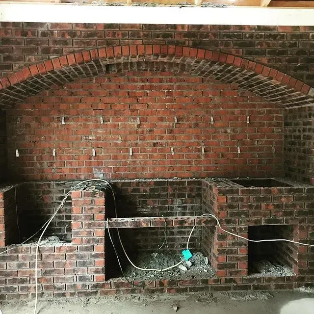 Brick fireplace alcove with a black metal grill, brick hearth, and hanging electrical cords