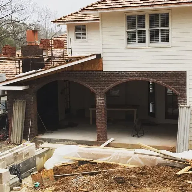 Two-story house under renovation with brick arches and a muddy construction site in front