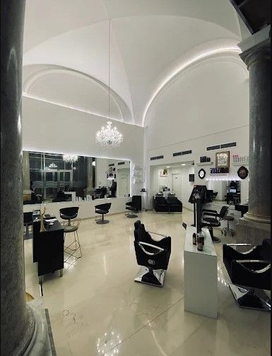Interno moderno di un salone di bellezza, interamente bianco, con poltrone da parrucchiere, specchi e soffitto a volta.