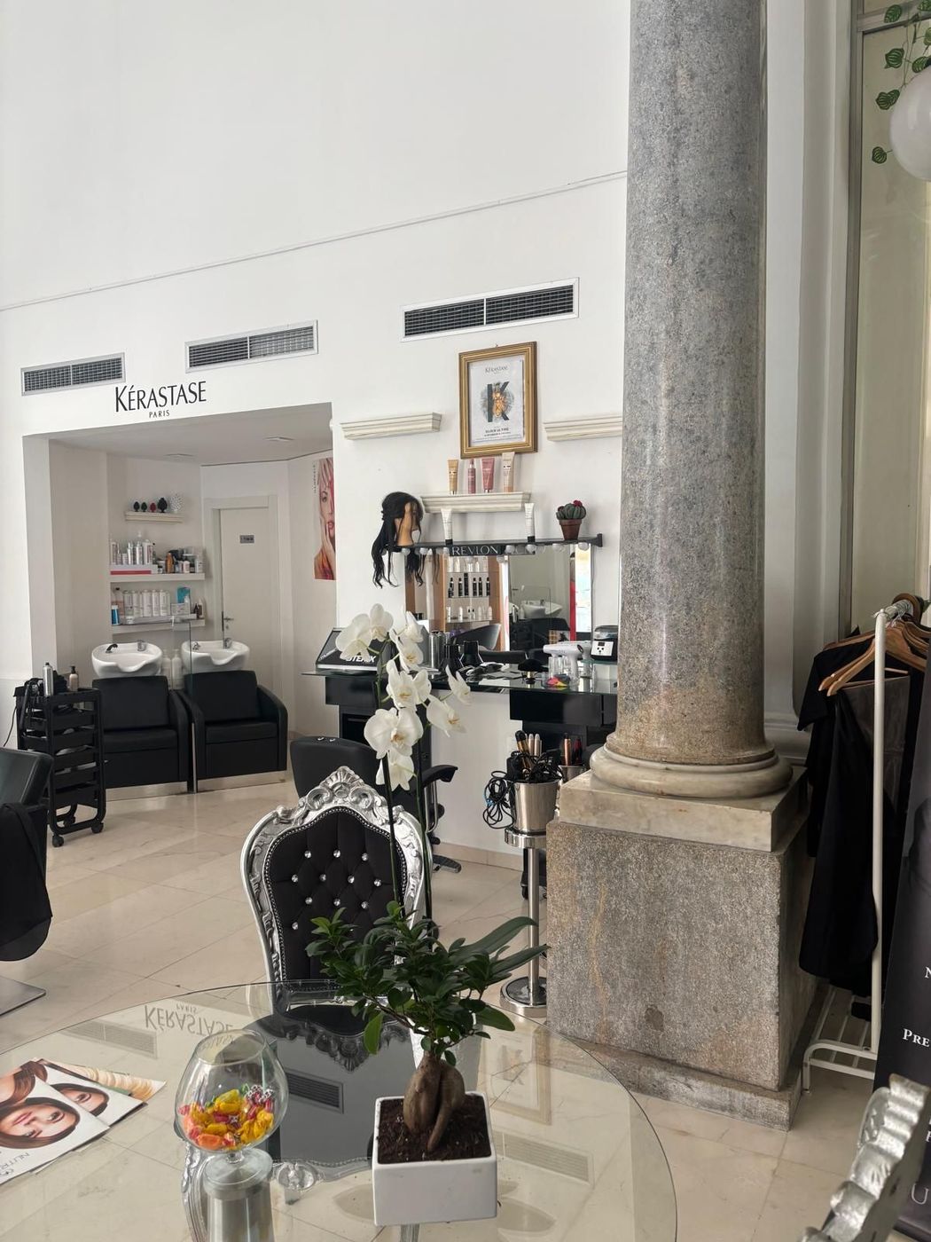 Interno di una boutique con arredi neri, una colonna in pietra e appendiabiti in uno showroom bianco e luminoso.