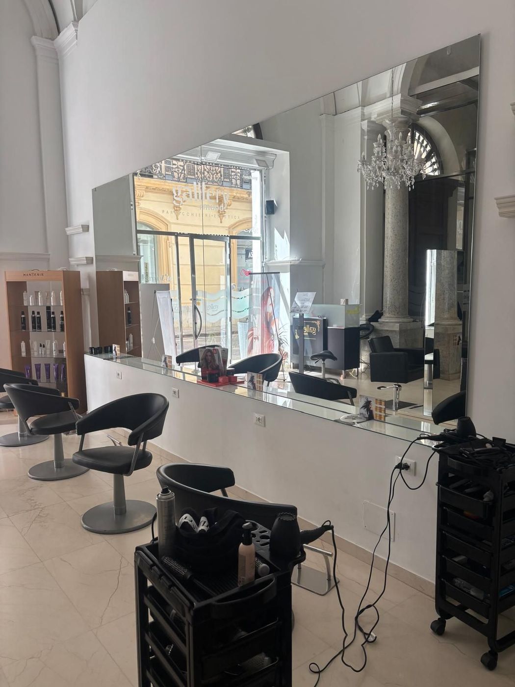 Interno di un salone da parrucchiere con poltrone per lo styling, specchi, banconi e postazione per la manicure, in una stanza luminosa.